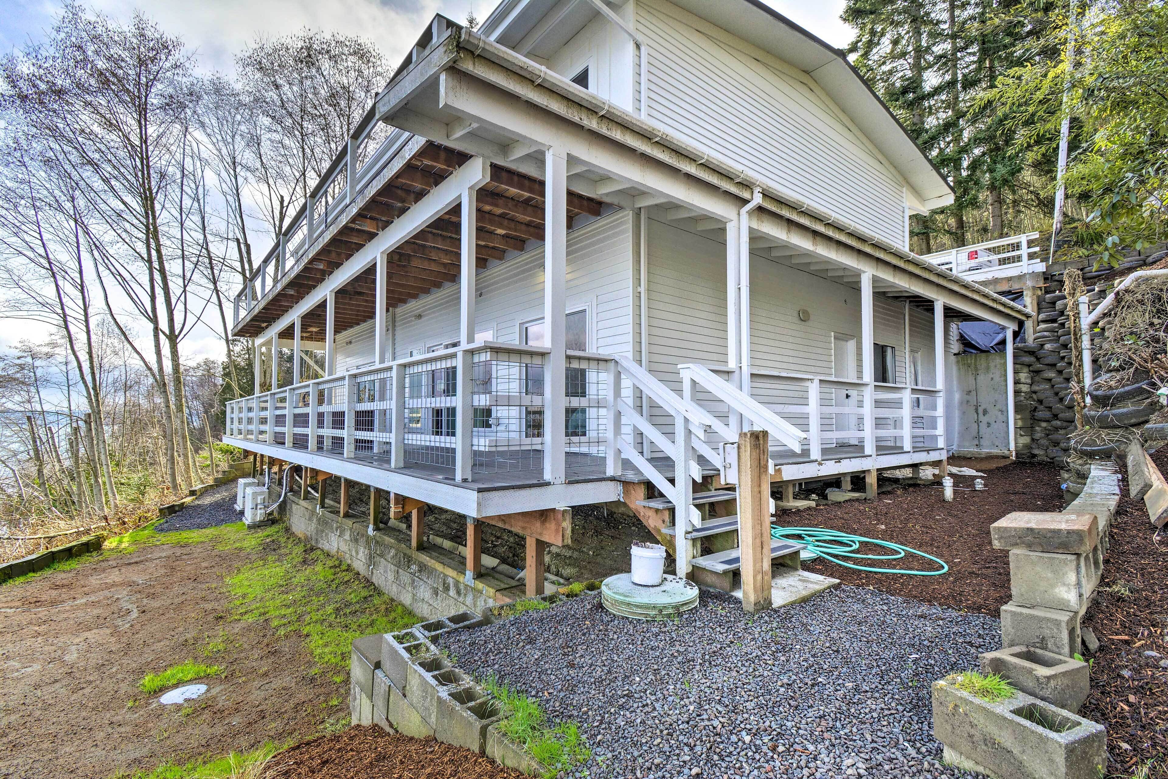 A two-story house with a covered porch, a stone retaining wall, and a view of the water.