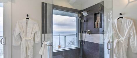 A modern bathroom with a glass-enclosed shower, a bathtub, and a window offering a view of the outdoors.
