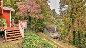 Una casa amb un porxo i escales que hi condueixen, envoltada de vegetació i arbres frondosos.
