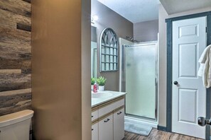 A bathroom with a wooden floor, a white toilet, a sink with a mirror, and a shower.