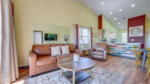 A spacious living area with a brown leather sofa, a round coffee table, and a dining table with yellow chairs. A kitchen with a colorful backsplash is visible in the background. - Vibrant Holiday Hills Resort Condo w/ Balcony (Branson)
