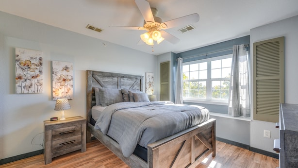 A bedroom with a wooden bed, a nightstand with a lamp, a ceiling fan, and a window with shutters. - Vibrant Holiday Hills Resort Condo w/ Balcony (Branson)