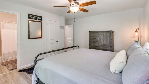 A bedroom with a bed, a ceiling fan, a wooden cabinet, and a wall-mounted mirror. - Waterfront Townville Home: Hot Tub & Lake Access! (Townville)