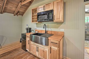 Una cocina compacta con armarios de madera, un lavamanos de acero inoxidable, un microondas negro y un horno empotrado.