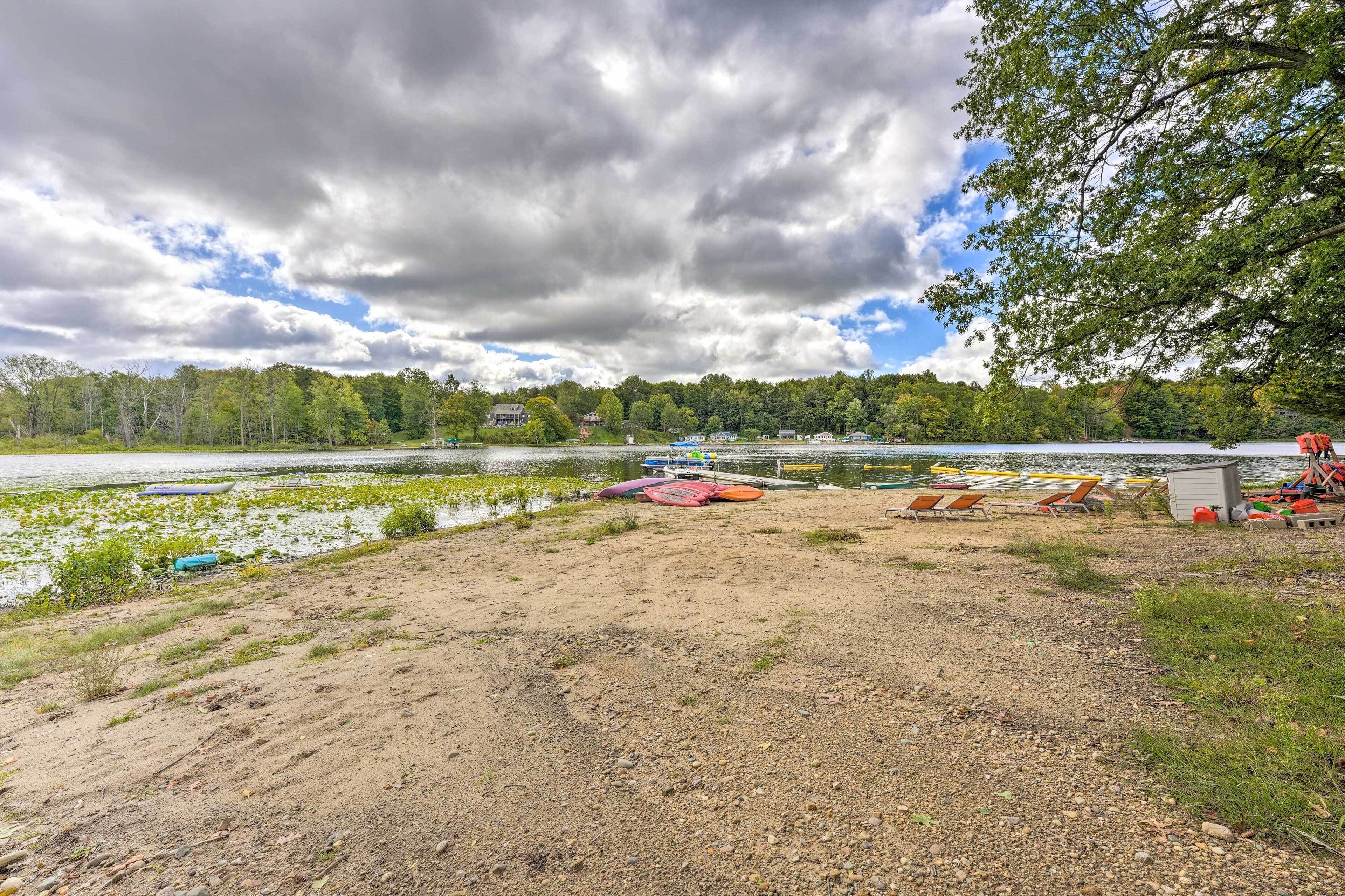 A lakeside area with boats, a sandy beach, and a forest in the background.