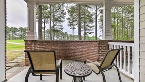 A covered patio with two chairs and a table, overlooking a brick wall and a grassy area with trees. - Resort-style Condo on Golf Course w/ Pool Access (Spring Lake)