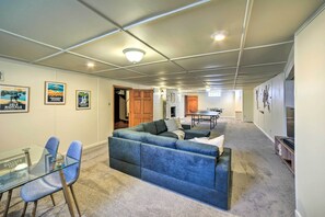 Een ruime woonkamer met een hoekbank, een glazen tafel met stoelen en ingelijste foto's aan de wanden.