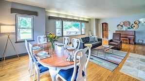 A dining area with a wooden table set for six, surrounded by white chairs. There is a sofa and a piano in the background. - Sugar Shores ~ 3 Mi to Indiana Dunes Nat'l Park (Chesterton)