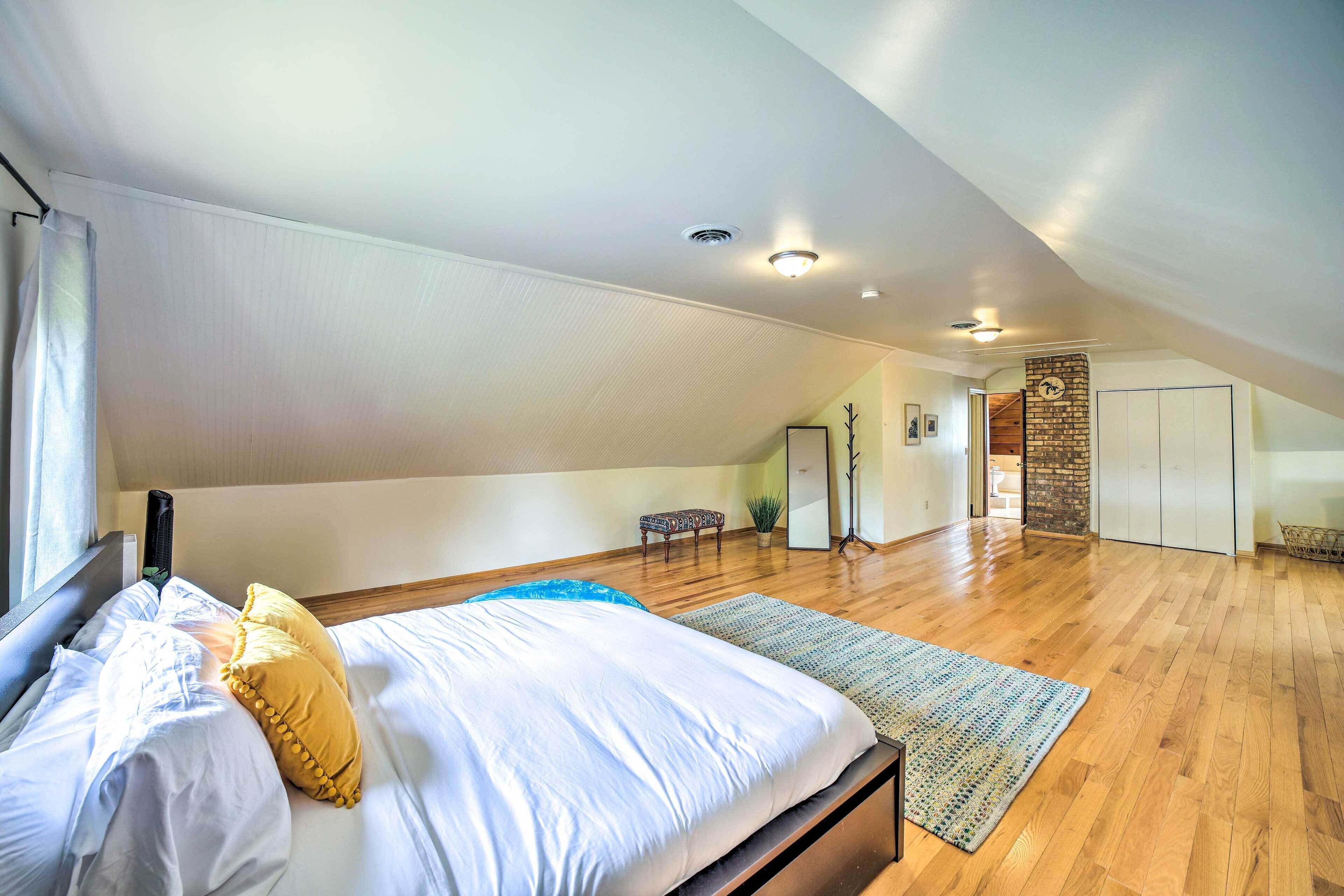 A bedroom with a large bed, a wooden floor, a small table, and a staircase leading to another room.