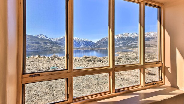 A room with a large window offering a view of a lake and mountains.