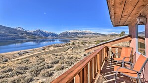 A wooden balcony with two chairs overlooking a lake and mountains.