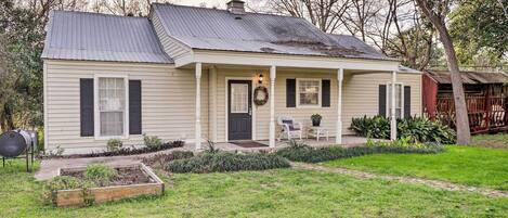 A single-story house with a front porch, a chimney, and a small garden area.