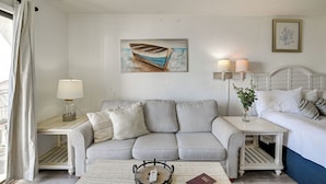 A room with a striped sofa, a bedside table with a lamp, a framed picture of a boat, and a bed with white bedding. - 4 Mi to Broadway at the Beach: Oceanfront Getaway (Myrtle Beach)