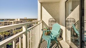 A balcony with a view of a parking lot and buildings, featuring a white railing, a table with chairs, and birdcages. - 4 Mi to Broadway at the Beach: Oceanfront Getaway (Myrtle Beach)