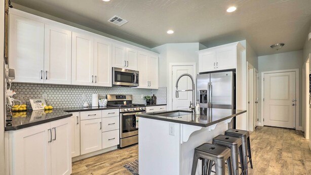 A modern kitchen with white cabinets, a central island, stainless steel appliances, and a hexagonal tile backsplash. - St George Area Townhome w/ Patio + Pool Access (Washington)