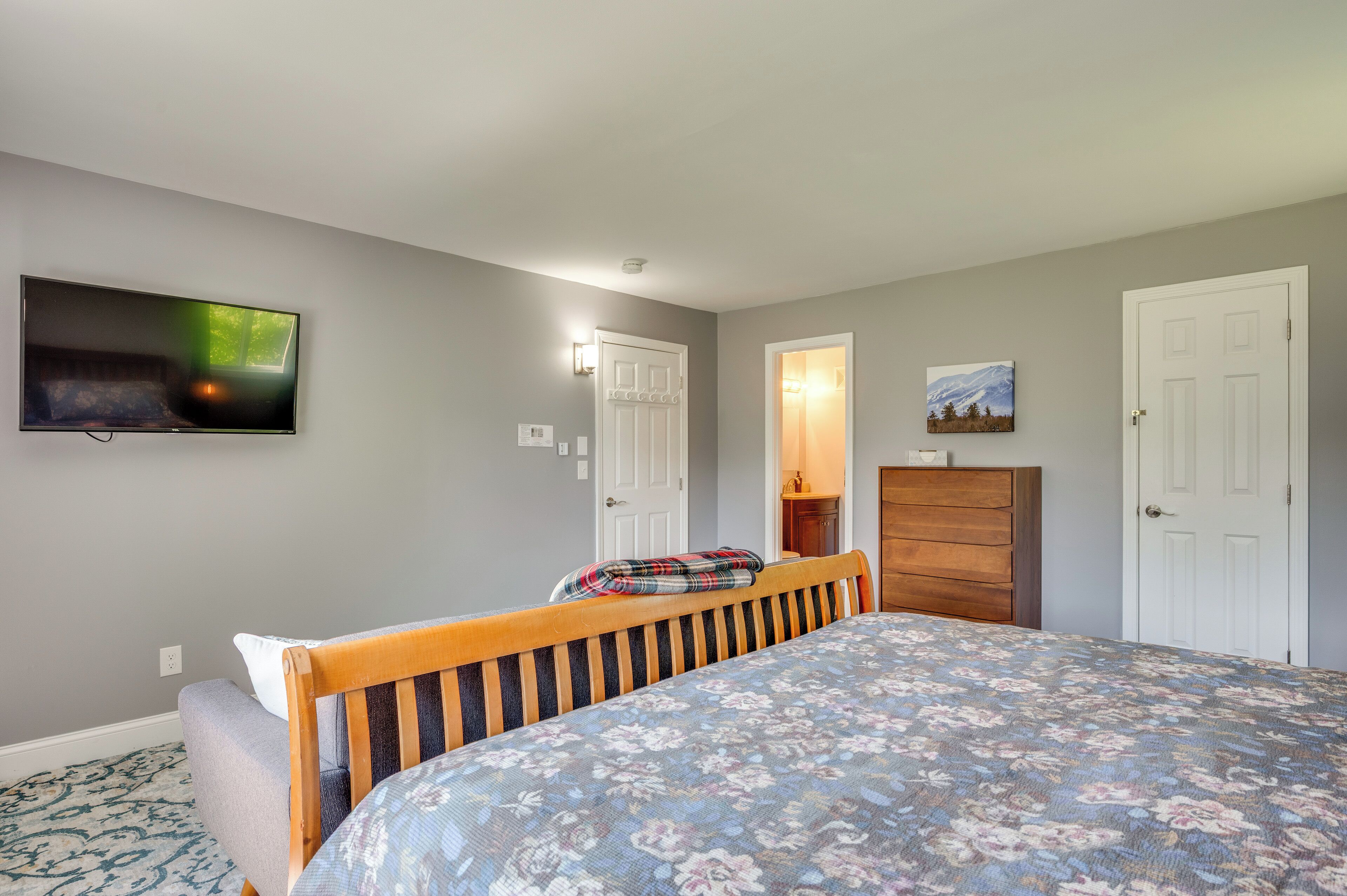 Un dormitorio con una cama, un televisor montado en la pared, un aparador y dos puertas.