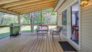 A covered deck with a grill, two wicker chairs, and a table. - Peaceful & Private Franconia Home by Cannon! (Franconia)