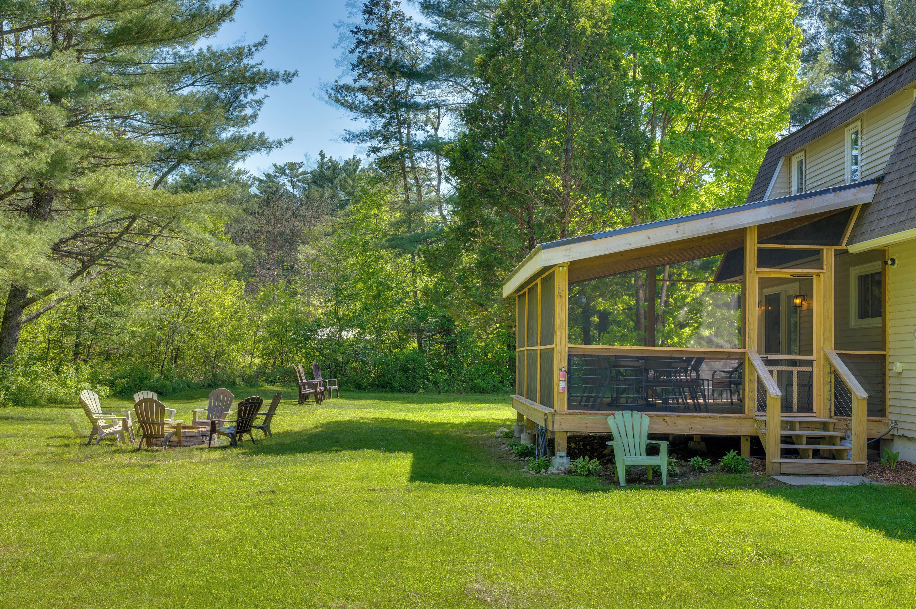 Une terrasse en bois, agrémentée de mobilier d’extérieur, entourée d’une pelouse verdoyante et luxuriante et de grands arbres.