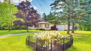 A residential house with a well-maintained lawn, a black metal fence, and flowering plants in the front yard. - Sunny Cloquet Home - 2 Mi to St. Louis River! (Cloquet)