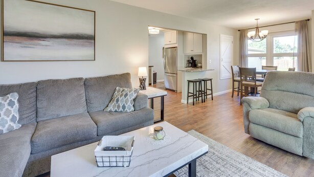 A modern living room with a grey sofa, a coffee table, and a dining area with a chandelier. - Sunny Cloquet Home - 2 Mi to St. Louis River! (Cloquet)