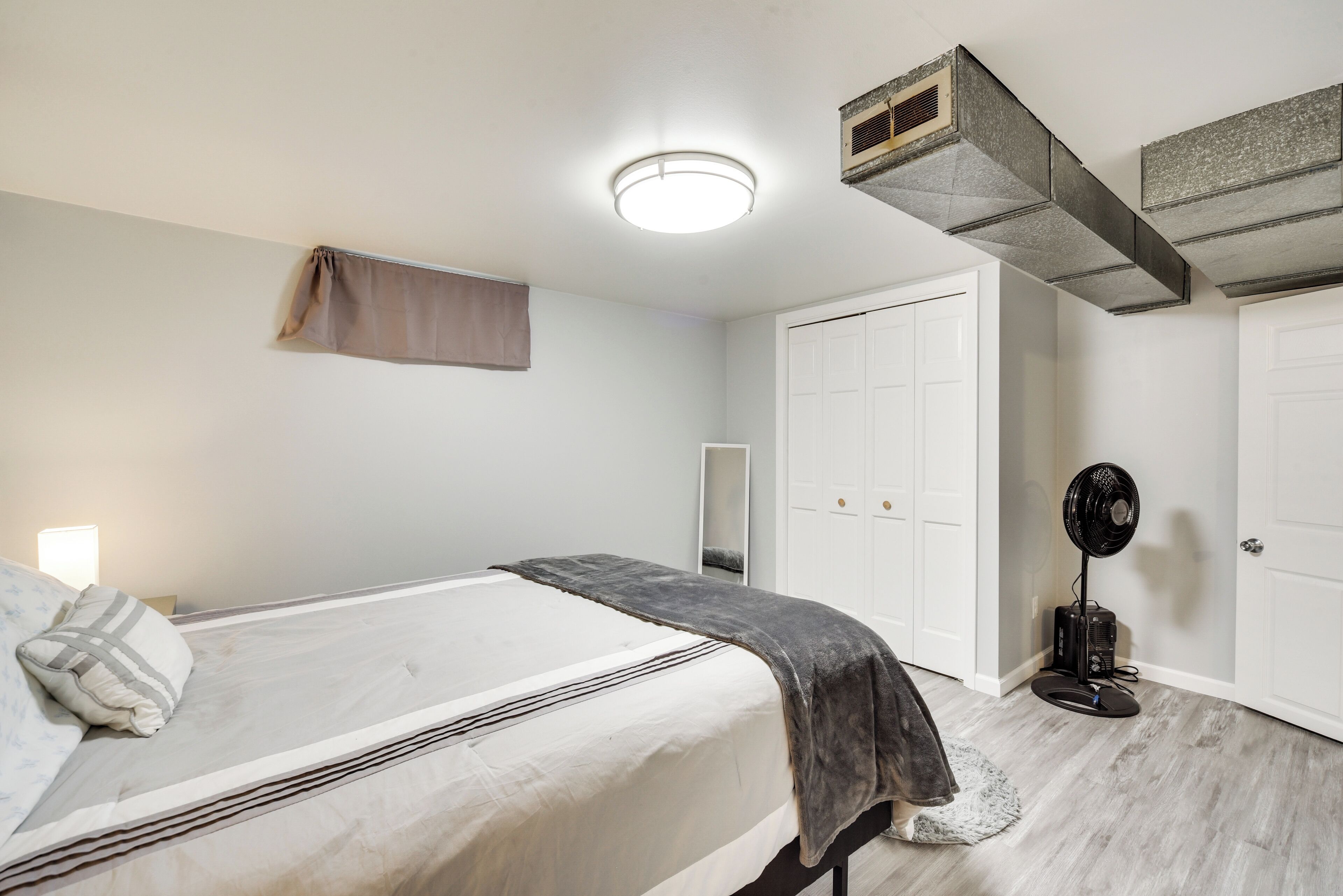 A bedroom with a bed, a bedside table, a mirror, a wardrobe, and a ceiling fan.