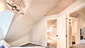 Une chambre avec un plafond en pente, un lit recouvert d’une couvre-lit à motifs floraux et un couloir menant à une autre pièce.
