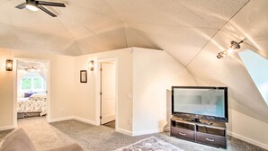 Une pièce avec un plafond en pente, un ventilateur de plafond, un téléviseur à écran plat posé sur un meuble, un tapis à motifs et une porte donnant sur une autre pièce.