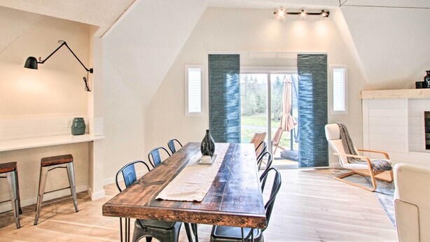 Un coin repas avec une table en bois, des chaises et une lampe. On peut admirer la vue sur l’extérieur à travers une porte vitrée.