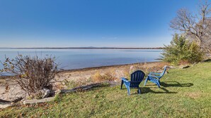 A lakeside view with two blue Adirondack chairs facing the water, surrounded by grass and a few trees. - Alburgh Lake House: Private Beachfront! (Alburg)