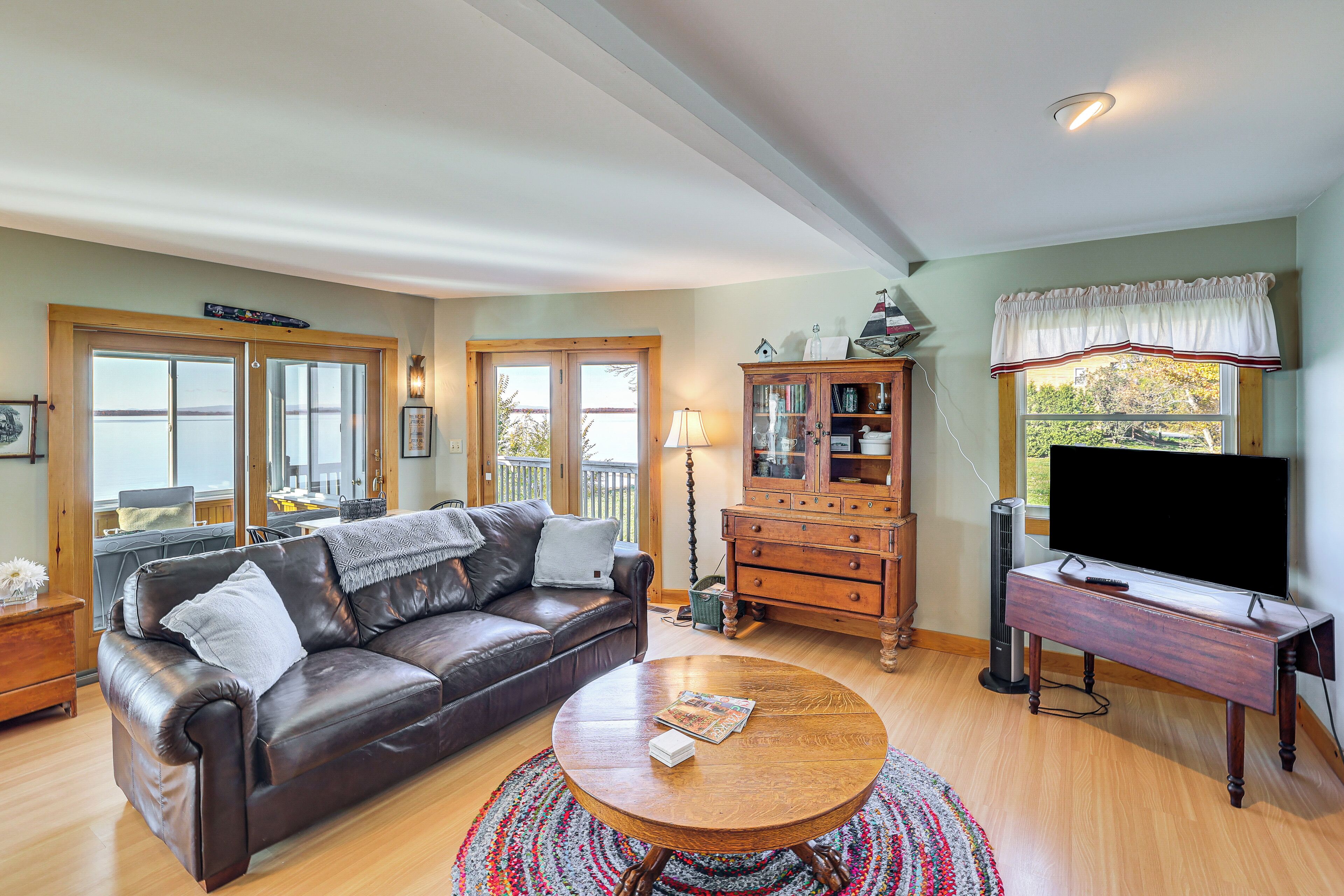 A living room with a leather sofa, a wooden coffee table, a television on a stand, and a large window with curtains.