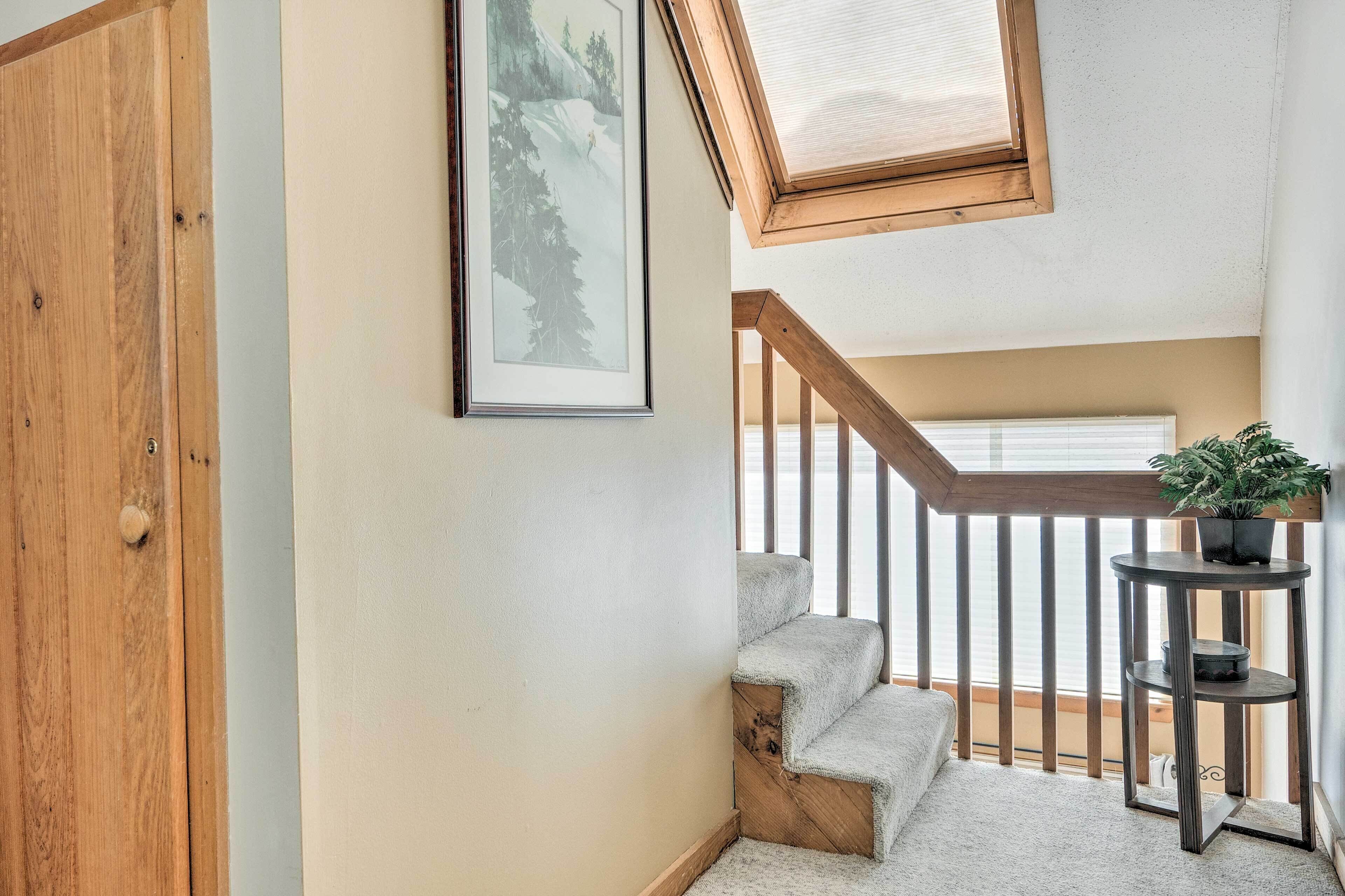 A staircase with a wooden handrail and carpeted steps leading to a landing. A framed picture hangs on the wall above the staircase.