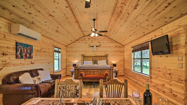 A cozy cabin interior with a wooden ceiling, a bed, a dining table with antlers, and a TV mounted on the wall. - Rustic-chic Country Cabin - 10 Mi to Main Street! (Fredericksburg)