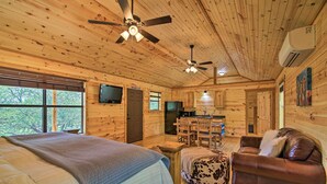 A cabin with wooden walls, a bed, a sofa, a dining table, and ceiling fans. - Rustic-chic Country Cabin - 10 Mi to Main Street! (Fredericksburg)