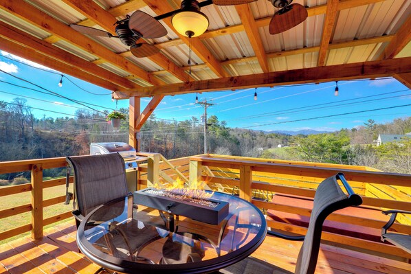 A wooden deck with a glass table and chairs, a grill, and a view of the surrounding landscape. - Studio w/ Loft, Hot Tub & Views in Marshall! (Marshall)