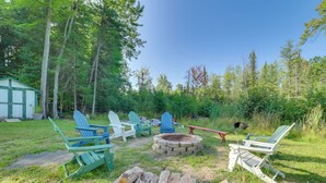 A backyard with Adirondack chairs, a fire pit, and a shed.
