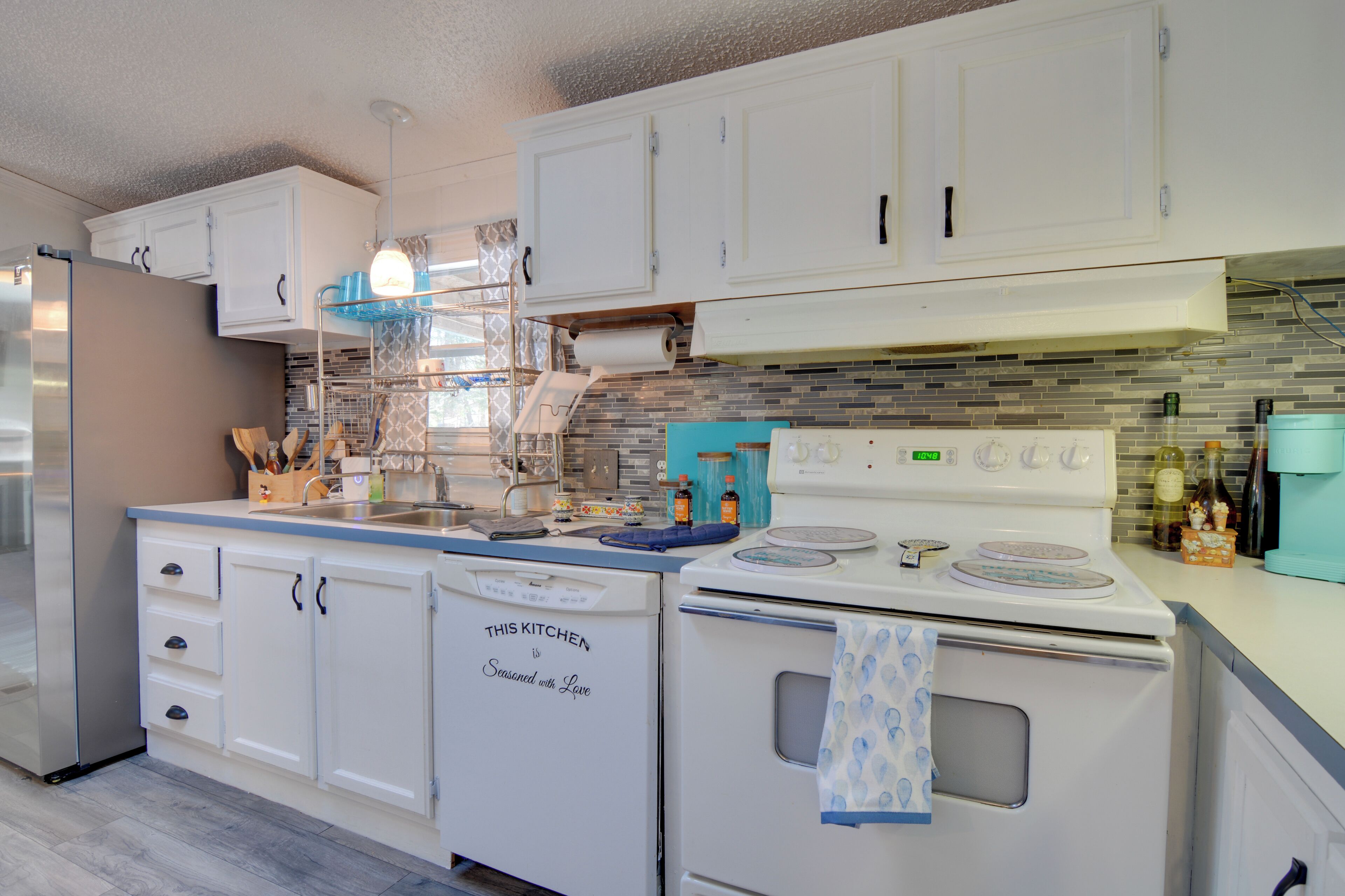 Een keuken met witte kasten, een roestvrijstalen koelkast, een witte kookplaat en een blauw aanrecht.