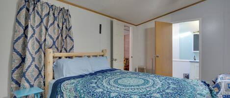 Un dormitorio con cama, cortinas, cabecera de madera, ventilador de techo y una puerta que da a otra habitación.