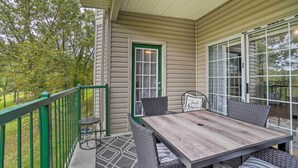 A covered outdoor patio with a table and chairs, a green door, and a view of trees.