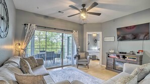 A spacious living room with a large sofa set, a ceiling fan, a flat-screen TV, and a sliding glass door leading to an outdoor patio.