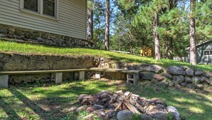 A stone retaining wall, a fire pit, and picnic benches in a backyard with trees and a house. - Lakefront Studio Cabin w/ Dock & Fire Pit! (Westfield)