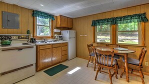 A kitchen with wooden cabinets, a white stove, a sink, and a dining table with chairs. - Lakefront Studio Cabin w/ Dock & Fire Pit! (Westfield)