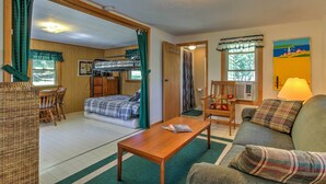 A cozy room with a bed, a sofa, a dining table, and a chair. There is a window with curtains, a lamp, and a painting on the wall. - Lakefront Studio Cabin w/ Dock & Fire Pit! (Westfield)