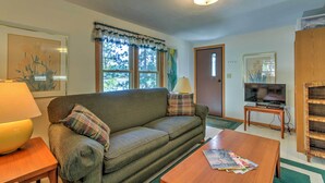 A cozy living room with a sofa, a coffee table, a TV, and a lamp. - Lakefront Studio Cabin w/ Dock & Fire Pit! (Westfield)