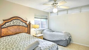 Ein Schlafzimmer mit einem Holzkopfteil, zwei Betten, einem Deckenventilator, einem Fenster mit Jalousien und einer Nachttischlampe.