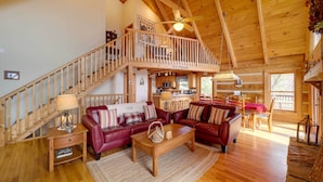 A spacious living area with wooden floors, a wooden staircase, and a balcony. - Smoky Mountain Vacation Rental w/ Large Deck! (Deep Gap)