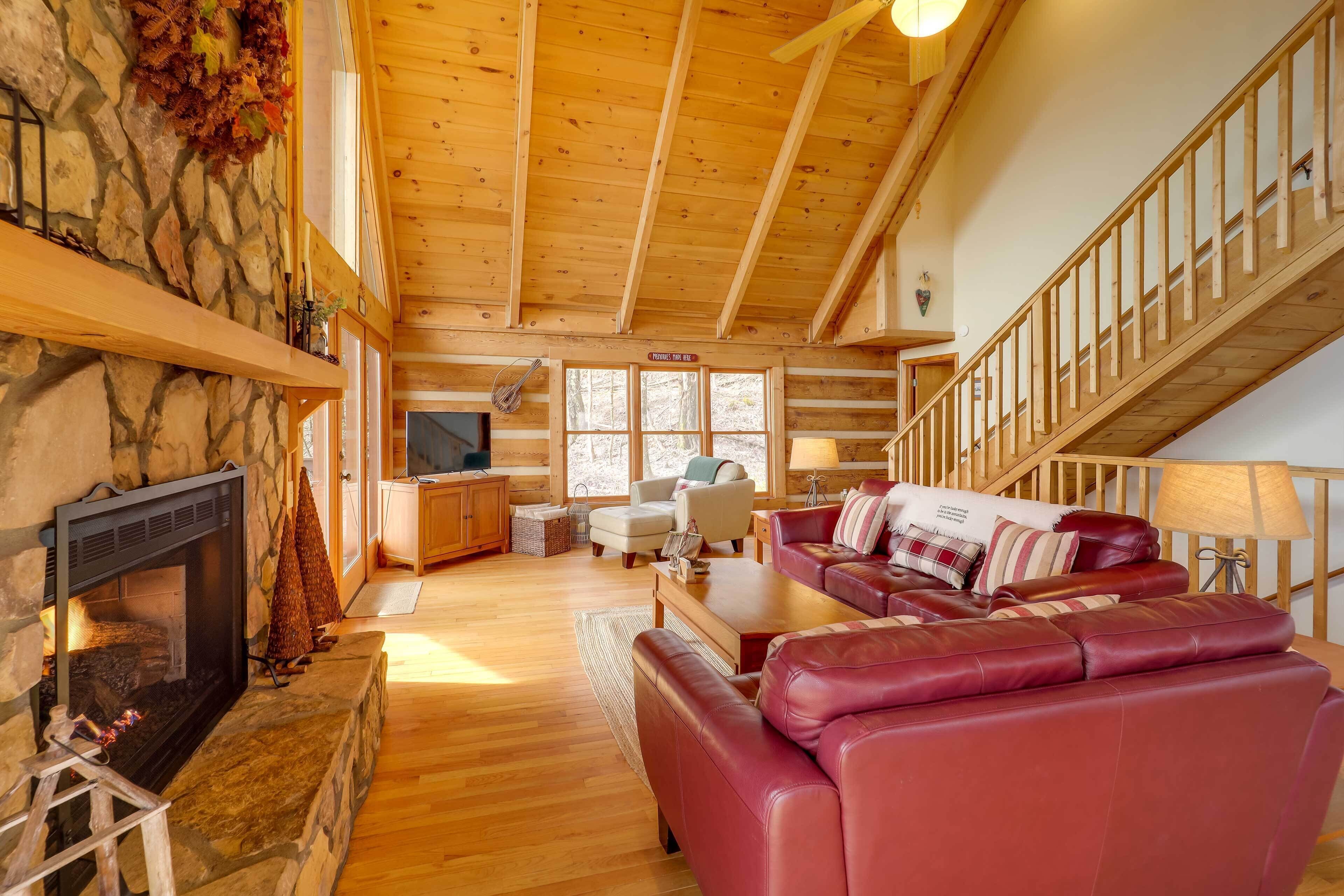 L’intérieur chaleureux d’un chalet avec une cheminée en pierre, un plafond en bois, un canapé en cuir rouge et un escalier.