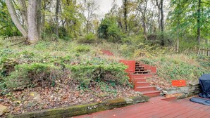 A wooden deck with a stone wall and a red staircase leading into a wooded area. - Cute Home w/ Patio ~ 7 Mi to Dtwn Pittsburgh (Pittsburgh)