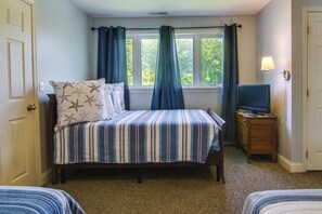 Quarto com cama, televisão sobre suporte de madeira e janela com cortinas.