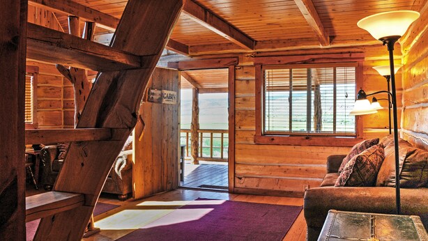 A cabin interior with a wooden staircase, a couch, and a lamp. - Remote Antimony Log Cabin w/ Green Meadow Views! (Antimony)
