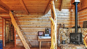 A log cabin interior with a stone fireplace, wooden walls, a ladder, and a rustic ambiance. - Remote Antimony Log Cabin w/ Green Meadow Views! (Antimony)